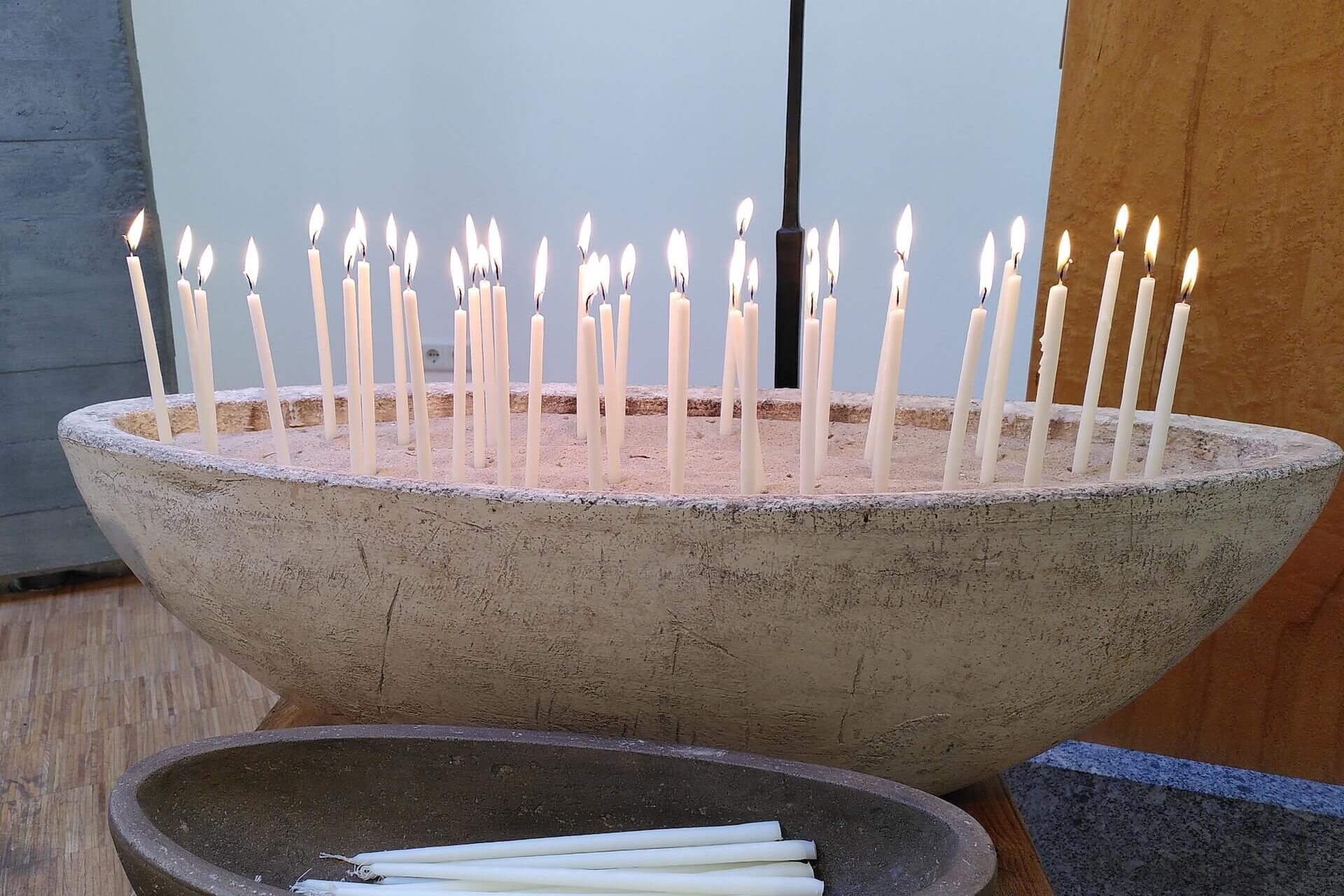 Ein Schiff aus Stein voller Kerzen, die im Sand stecken: ein schönes Ritual für Erinnerungen und Dankbarkeit bei einer freien Trauerfeier.