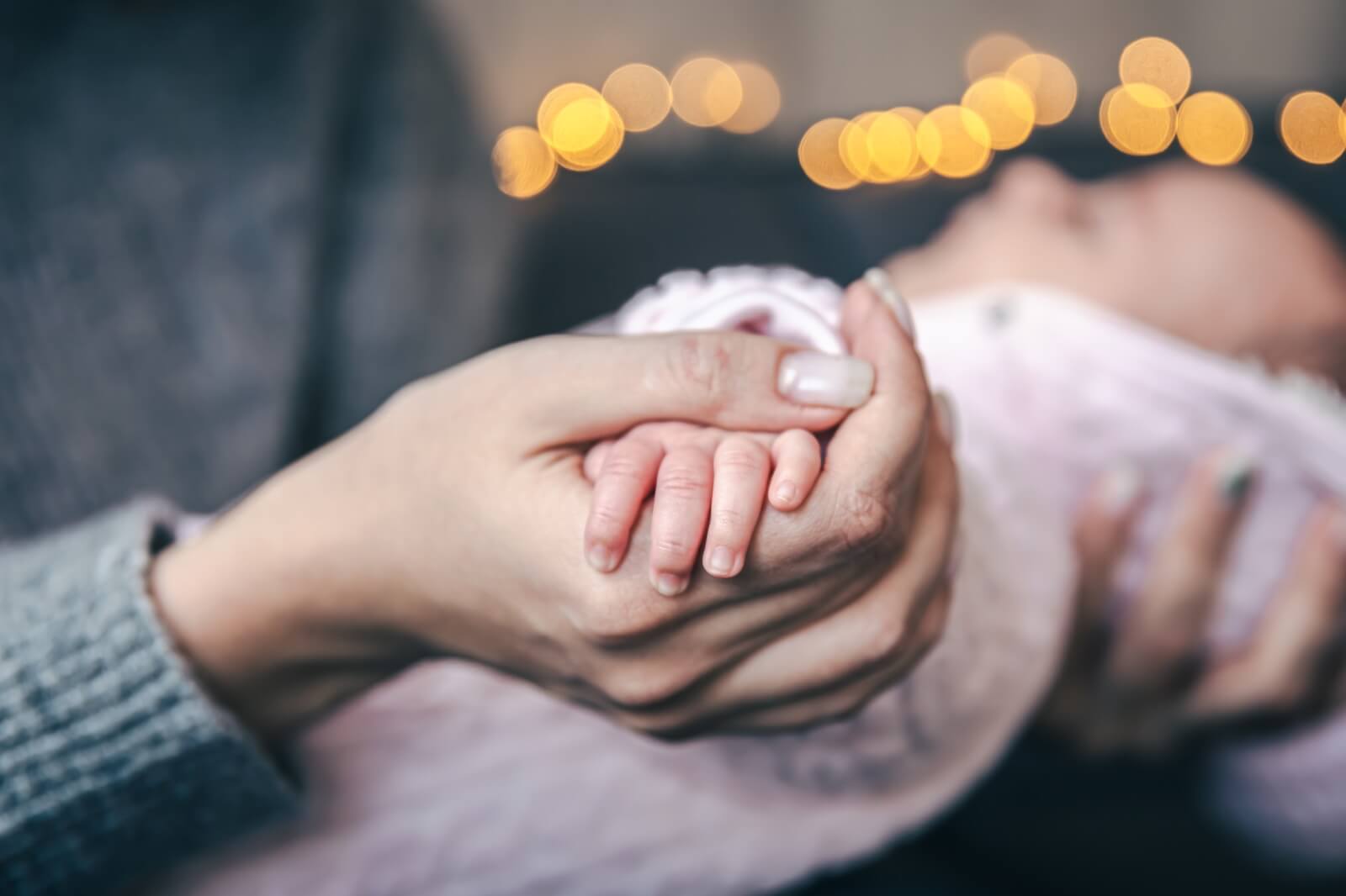 Dankbar für die Geburt des Neugeborenen: Beim Willkommensfest und der Segensfeier hält die Mama die Hand ihres Babys liebevoll fest.